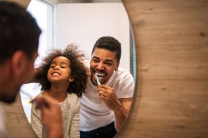 Father and daughter brusing teeth and smiling in front of mirror