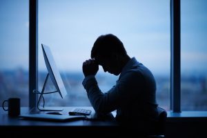 Man supporting head in hands over a laptop